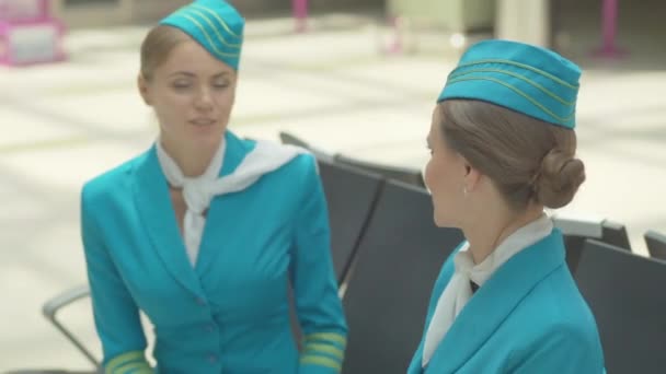 Regálové zaměření se mění z sebevědomé letušky na krásnou mladou bělošku v modré uniformě, která mluví s kolegyní v čekárně na letišti. Profesionálové chatují v terminálu a usmívají se. — Stock video