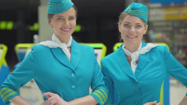 Hermosas mujeres delgadas y confiadas en uniforme de azafata posando en la terminal del aeropuerto. Retrato de hermosas azafatas caucásicas de pie en la terminal, mirando a la cámara y sonriendo. — Vídeos de Stock