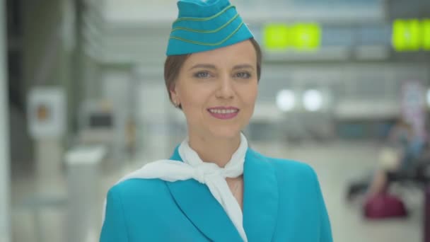 Smiling beautiful Caucasian stewardess sending air kiss at camera. Portrait of charming mid-adult woman posing in airport. Professional flight attendant standing in terminal before departure. — Stock Video