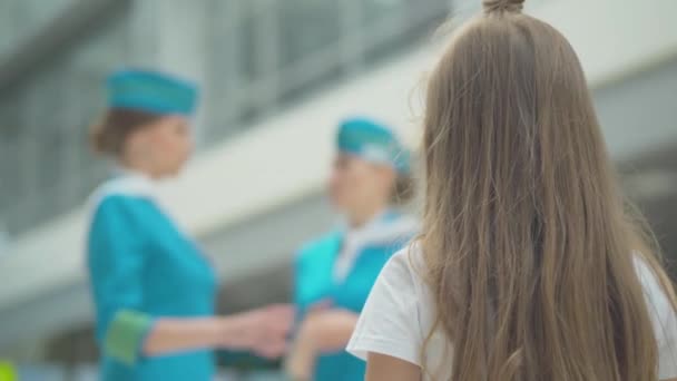 Vista posteriore della bambina bruna che guarda hostess sfocate che parlano nel terminal dell'aeroporto. Primo piano del bambino caucasico che ammira assistenti di volo professionisti prima della partenza. Sognare, turismo. — Video Stock