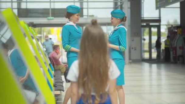 Two confident stewardesses talking in airport with blurred little girl looking at them. Back view of unrecognizable child admiring professional Caucasian flight attendants in terminal. — Stock Video