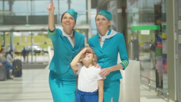 Очаровательная маленькая девочка, стоящая рядом со стюардессами и смотрящая на взлет самолета. Портрет счастливого кавказского ребенка, наслаждающегося солнечным днем с профессиональными стюардессами перед отъездом. — стоковое видео
