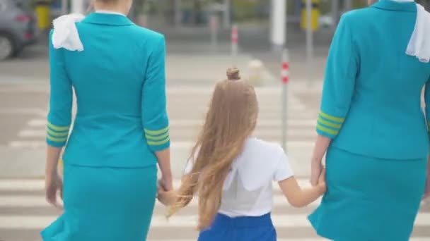 Bakåt av liten flicka promenader till flygplatsen grindar hålla händerna på flygvärdinnor. Professionella medföljande flygvärdinnor som förföljer barn för avgång. Begreppet luftfartsregler. — Stockvideo