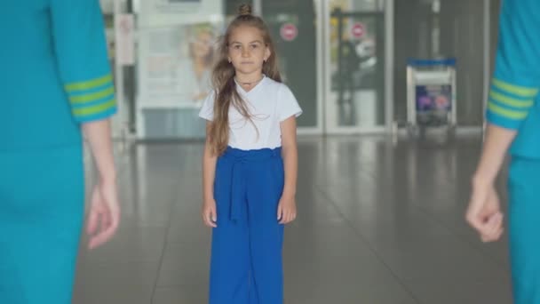 승무원을 찬양하는 백인 여자 애가 공항에 들어가서 카메라를 보고 있어요. 귀여운 아이가 해외로 떠나길 기다리고 있는 모습. 승무원이 되려는 꿈. — 비디오