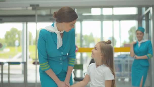 Charmig glad kvinna i flygvärdinna uniform pratar med söt liten vit flicka på flygplatsen. Porträtt av vacker flygvärdinna medföljande barn i internationell resa. — Stockvideo