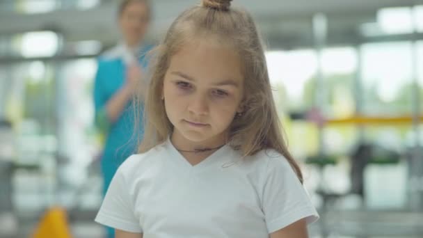 Primer plano de la niña triste de pie en la terminal del aeropuerto con azafata borrosa de pie en el fondo. Retrato de hija molesta esperando a la azafata. Trabajo de turismo internacional. — Vídeo de stock