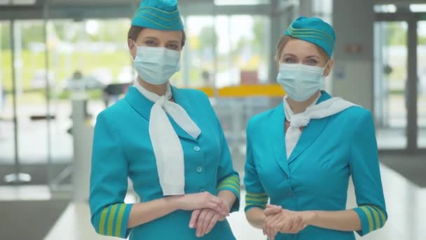 Retrato de dos azafatas profesionales confiadas en máscaras faciales paradas en el aeropuerto mirando la cámara. Mujeres caucásicas jóvenes en uniforme de azafata posando antes de la salida en la pandemia de Covid-19. — Vídeos de Stock