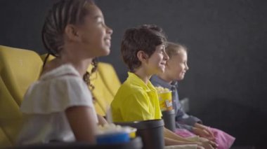 Orta Doğulu şirin bir çocuğun arkadaşlarıyla sinemada çizgi film izlemesinin yan görüntüsü. Çok ırklı çocuklar sinemada sinemadan zevk alıyorlar. Kaygısız çocuklar sarı sandalyelerde oturuyor ve gülüyorlar..