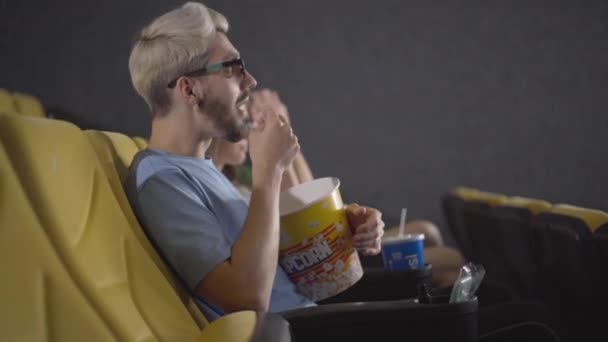 Vista lateral del hombre caucásico relajado en gafas 3D viendo películas en el cine y comiendo palomitas de maíz. Retrato de un chico guapo y despreocupado disfrutando de la comedia. Concepto de ocio y entretenimiento. — Vídeos de Stock