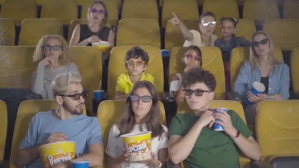 Portrait de spectateurs heureux au cinéma mangeant du pop-corn et bavardant. Groupe d'hommes, de femmes, de garçons et de filles insouciants et détendus regardant des films en 3D. Des amis joyeux parlent devant et sourient. — Video