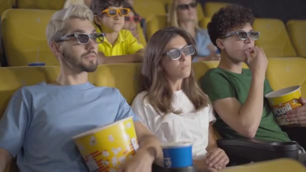 Angle view of absorbed people watching 3d film in cinema as young woman receiving phone call. Portrait of rude Caucasian lady answering and disturbing visitors in movie theatre. — Stock Video