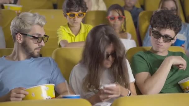 Beautiful young woman picking up phone in cinema distracting people from film. Portrait of brunette Caucasian lady disturbing audience in movie theatre. Rules violation, politeness. — Stock Video