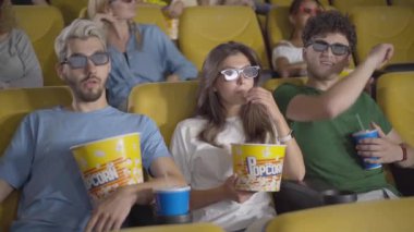 Romantik genç adam sinemada kadınlara sarılıyor. Sinema salonunda sevgili olan beyaz bir çiftin açısı. Alaycı adam 3D gözlükten sevgili sevgilisine bakıyor..