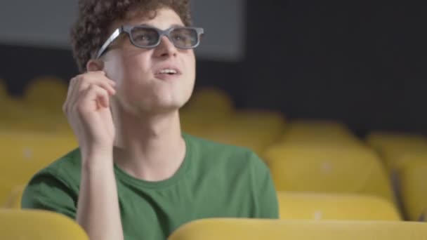 Primer plano del joven hombre alegre viendo películas en 3D en el cine. Retrato de visitante caucásico absorbido alegre con pelo rizado y ojos marrones bajando gafas 3d y sonriendo. — Vídeos de Stock