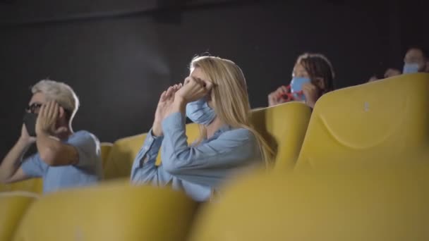 人们在电影院里看关于考罗纳维病毒大流行的电影。戴面具的男女坐在一起保持社会距离的视角。电影爱好者戴上3D眼镜，看着屏幕. — 图库视频影像