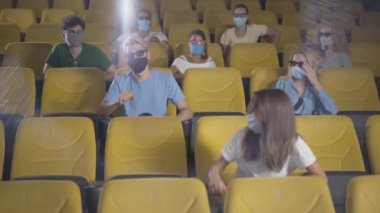 Covid-19 salgınında maskeli bir adam sinemada öksürüyor. Sinema salonundaki hastalardan uzaklaşan insanlar. Koronavirüs karantinasında film izleyen mahcup genç adama kamera yaklaşıyor..