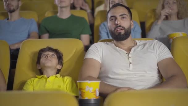 Joyeux homme et garçon du Moyen-Orient regardant un film au cinéma et parlant. Portrait de père et fils heureux appréciant les week-ends au cinéma. Concept de paternité et de lien. — Video