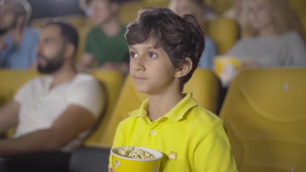 Schattige jongen uit het Midden-Oosten met een stil gebaar in de bioscoop. Portret van een gelukkig kind dat geniet van de film in de bioscoop. Knap krullend kind met vinger op de lippen en kijkend naar de camera. — Stockvideo