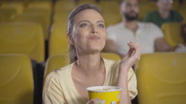 Sinemada film izleyen heyecanlı orta yaşlı beyaz kadın portresi. Şaşırmış bir yüz ifadesiyle. Sinema salonunda hafta sonları eğlenen güzel, içine kapanık bir bayan. Patlamış mısır yiyen çekici bir kadın..