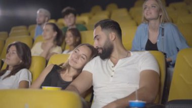 Sinemada yakışıklı Orta Doğulu bir adamla çıkan neşeli beyaz kadın portresi. Mutlu çift sinemada heyecan verici filmler izliyor, patlamış mısır yiyor ve konuşuyor..