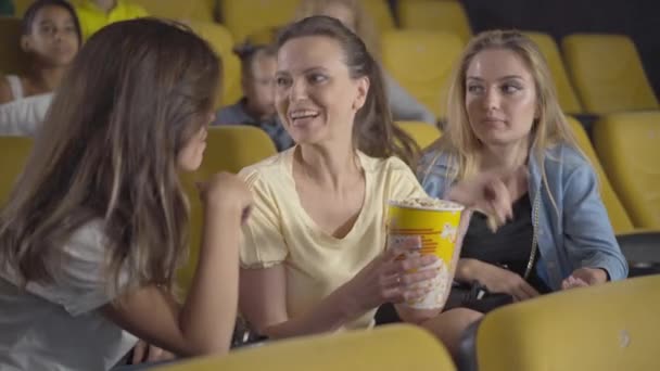 Eccitato donna caucasica mangiare popcorn e discutere commedia con gli amici. Ritratto di giovani donne allegre che guardano film al cinema e parlano. Gioioso giovani signore riposo in cinema su — Video Stock