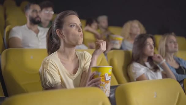 Portrait de femme blanche absorbée regardant un film passionnant au cinéma et mangeant du pop-corn. Vue d'angle d'une visiteuse absorbée jouissant d'une première au cinéma avec une expression faciale choquée. — Video
