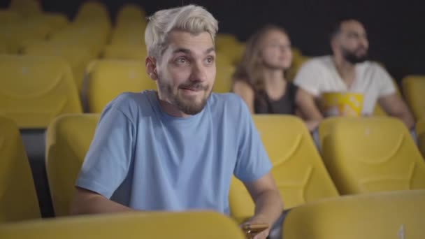 Junger kaukasischer Mann beim Fotografieren der Leinwand im Kino. Porträt eines gutaussehenden Verbrechers, der die Regeln des Kinos bricht. Skrupellose Typen, die Filme gucken und das Smartphone benutzen. Verderbendes Konzept. — Stockvideo