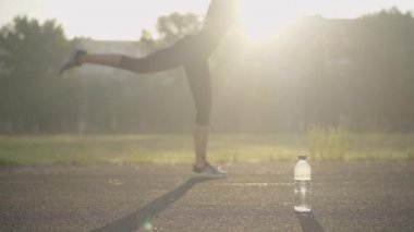 Bulanık ince sportmen kadın güneş ışığında sabah egzersizi yapıyor. Önünde bir şişe ferahlatıcı su duruyor. Atletizm sahasında güneşin doğuşunda kendine güvenen beyaz kadın antrenmanı.