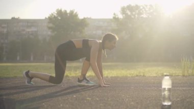 Güneş ışınlarıyla kaçan kendine güvenen beyaz kadın sporcunun yan görüntüsü. İnce, güzel bir kadının portresi yaz sabahı açık havada spor sahasında koşuyor. Gün doğumunda genç bayan koşucu eğitimi.