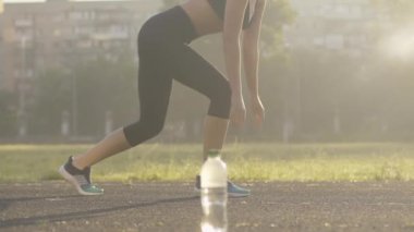 Konsantre beyaz kadın sporcu yaz sabahı atletizm sahasında koşmaya başlıyor. Güneş doğarken açık havada koşan kendine güvenen beyaz zayıf kadının yan görünümü..