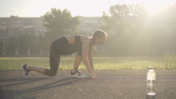 Zijaanzicht van zelfverzekerde blanke sportvrouw die wegrent in zonnestralen. Portret van slanke mooie vrouw joggen op sportveld buiten op de zomerochtend. Jonge vrouwelijke loper training bij zonsopgang. — Stockvideo