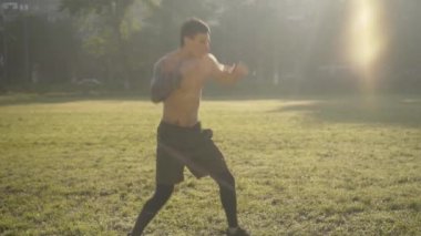 Kafkas sporcusu güneş ışığında boks gölgesinin geniş açılı görüntüsü. Gün doğumunda dışarıda boksörlerin antrenmanlarının yan görüntüsü. Atletik yakışıklı bir adamın portresi. Yaz sabahı dışarıda egzersiz yapıyor..