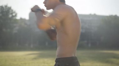 Avcı uçuşu eğitiminin ortası açık havada. Güneş ışınlarıyla boks yapan kendine güvenen beyaz adamın yan görüntüsü. Yaz sabahı spor yapan güçlü bir sporcunun portresi..
