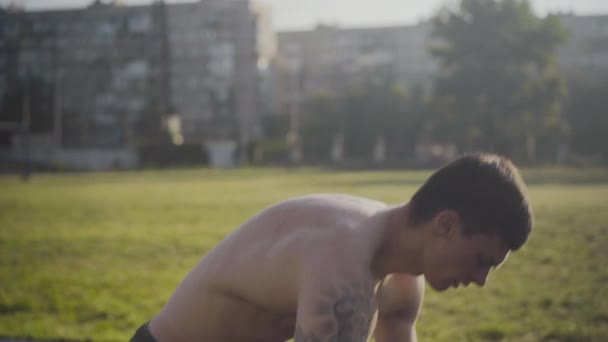 Ung självsäker man börjar springa på stadion i solljus. Sidovy över stark tatuerad idrottsman jogga på sommaren morgon utomhus. Porträtt av vit löpare utbildning på stadion vid soluppgången. — Stockvideo