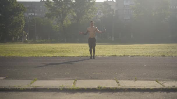 极宽的镜头,白人运动员在阳光下跳绳.夏天早上在户外训练的年轻运动员的画像。强壮的运动员在体育场日出时锻炼. — 图库视频影像