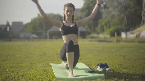 Hermosa mujer caucásica con colas de caballo de pie en posición de yoga en la esterilla de ejercicio. Retrato de deportista segura y concentrada entrenando al aire libre en la mañana de verano. Deporte y meditación. — Vídeos de Stock