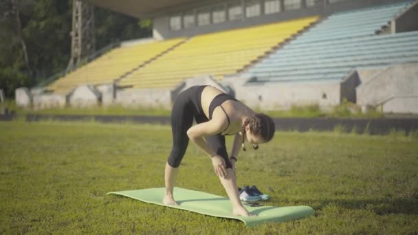 Ampio colpo di flessibile giovane donna in piedi in posa yoga sul tappeto esercizio. Ritratto di bello yogi caucasico magro che si esercita all'aperto in estate mattina. Stile di vita sano e allenamento. — Video Stock