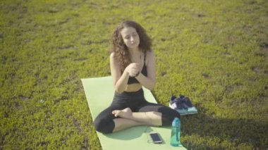 Egzersiz minderinde oturup ısınan neşeli beyaz kadın manzarası. Kulaklıkla müzik dinleyen zayıf bir kadının portresi yaz sabahında gün ışığında antrenman gibi..