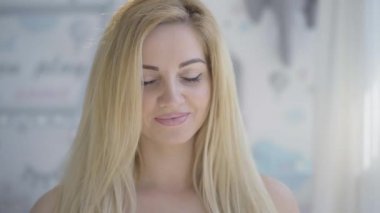 Kamera mutlu beyaz kadının gülümseyen suratından hamile karnına doğru kayıyor. Bebek bekleyen sarışın güzel annenin portresi. Annelik ve annelik.