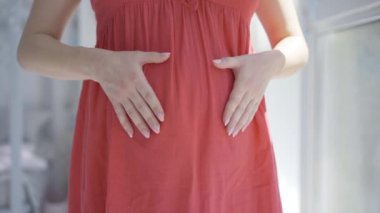 Tanınmaz bir beklenti, elleri hamile karnında kalp şeklinde. Sevgi dolu bir bebek bekleyen mutlu beyaz kadın. Çocuk bekleyen genç bir bayan. Kadınlık ve annelik.