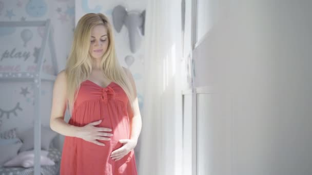 Portrait of happy pregnant woman standing at home and smiling. Positive dreamy Caucasian lady enjoying pregnancy indoors. Future mother dreaming about childbirth. Motherhood concept. — Stock Video