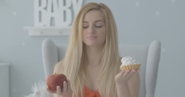 Mladá blonďatá běloška držící jablko a dort. Portrét krásné dámy, jak natahuje zdravé jídlo na kameru a usmívá se. Regálové zaměření se mění z obličeje na plody zdravé. Cinema 4k ProRes HQ. — Stock video