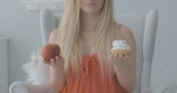 Sağlıklı kırmızı elma yerine kremalı keki seçen tanınmamış genç bir kadın. Rack odak noktası hamile bir kadından kameraya gerilmiş tatlı bir fırına dönüşüyor. Hamilelik diyeti. Sinema 4k ProRes Merkezi. — Stok video
