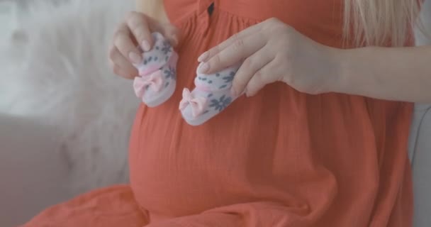 Close-up de jovens mãos femininas caucasianas segurando botas de bebê e imitando pisar na barriga grávida. Mulher grávida irreconhecível desfrutando da gravidez. Cinema 4k ProRes HQ. — Vídeo de Stock