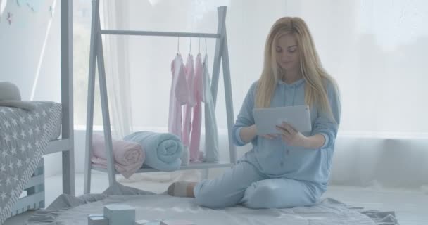 Porträt einer glücklichen Schwangeren mit Tablet und anrührender Kinderkleidung, die am Kleiderbügel hängt. Lächelnde kaukasische erwartungsvolle Online-Einkäufe vor der Geburt. Bequemer Einkauf. Cinema 4k ProRes Hauptquartier. — Stockvideo