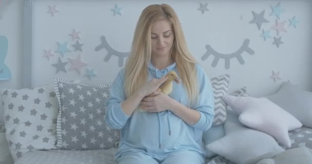 Очаровательная счастливая женщина гладит жёлтого утёнка. Портрет беременной белой женщины, играющей с уткой в спальне. Веселый будущий веселится в помещении. Штаб-квартира кинотеатра 4k ProRes. — стоковое видео