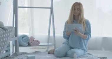 Tablet kullanan gülümseyen hamile bir kadın ve askıda çocuk kıyafetleri var. Doğumdan önce internetten alışveriş yapan kendinden emin beyaz adamın mutlu portresi. Sinema 4k ProRes Merkezi.