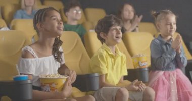 Sinemada film izleyen heyecanlı çocuklar ve arka planda filmlerden zevk alan yetişkinler. Mutlu ziyaretçilerin portresi patlamış mısır yiyor ve gülümsüyor. Sinema 4k ProRes Merkezi.