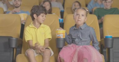 Sinemada film seyreden ve patlamış mısır yiyen çocuklar. Kaygısız Orta Doğulu bir erkek ve arka planda bulanık insanların olduğu sinemadan zevk alan beyaz bir kız portresi. Sinema 4k ProRes Merkezi.