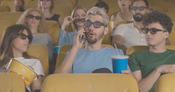 Portret van een onbeschofte jongeman aan de telefoon in de bioscoop die mensen negeert. Bezoekers die een blanke man uitschelden die lawaai maakt in de bioscoop. Ill-mannered man met 3D-bril. Cinema 4k ProRes Hoofdkwartier. — Stockvideo